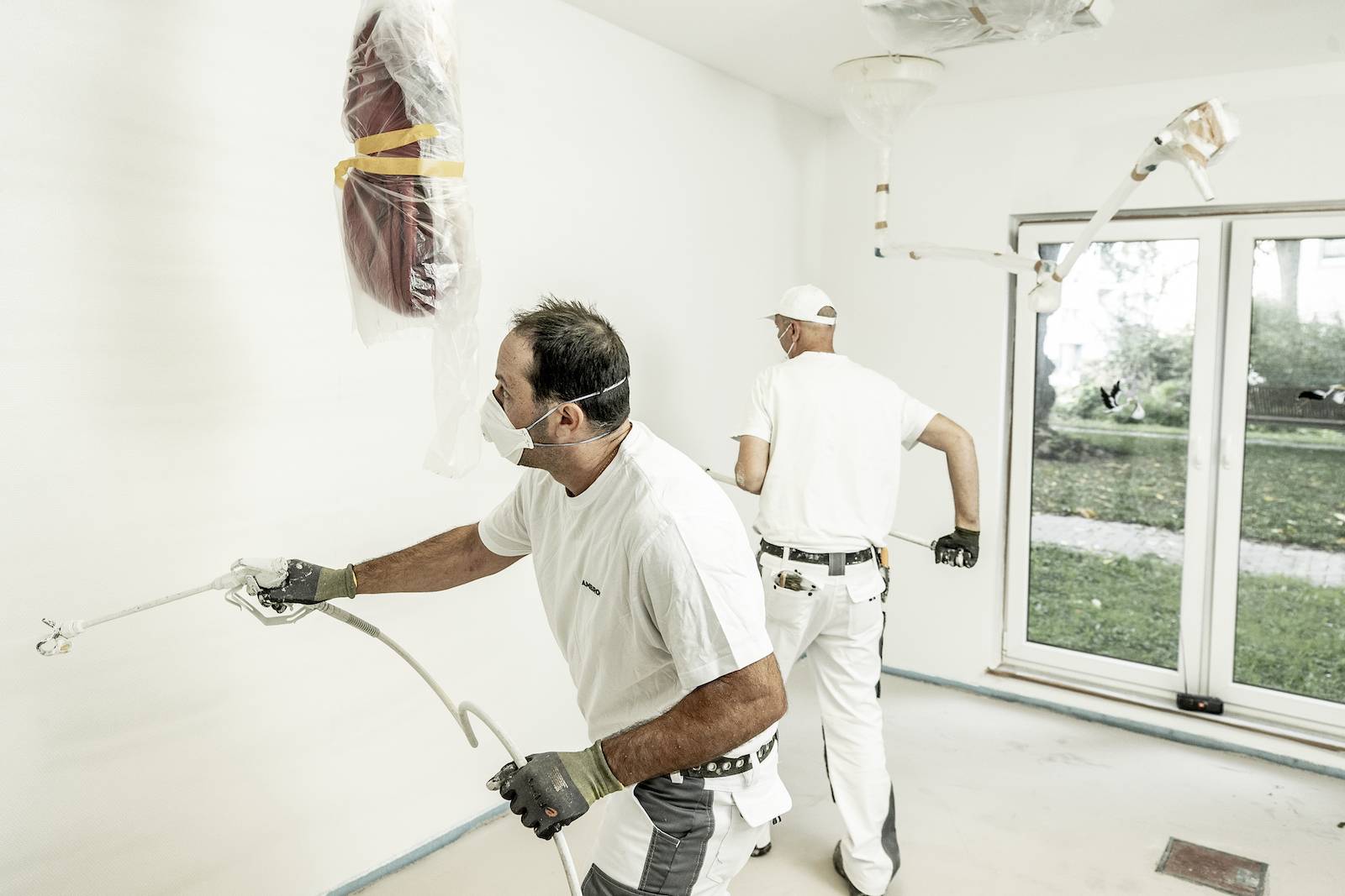 Zwei Maler streichen eine Wand in einem Raum.