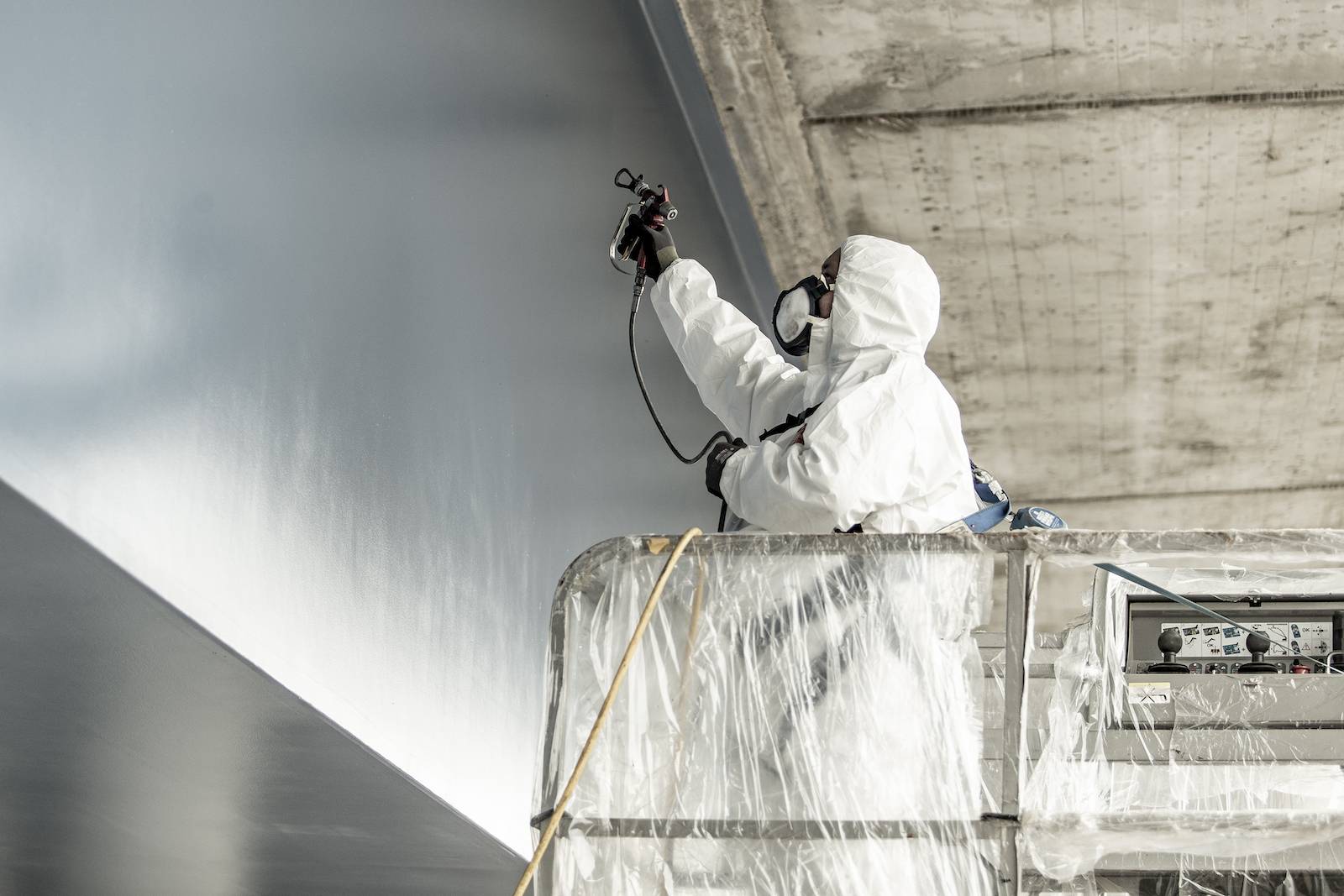 Maler in Schutzkleidung sprüht eine Wand.