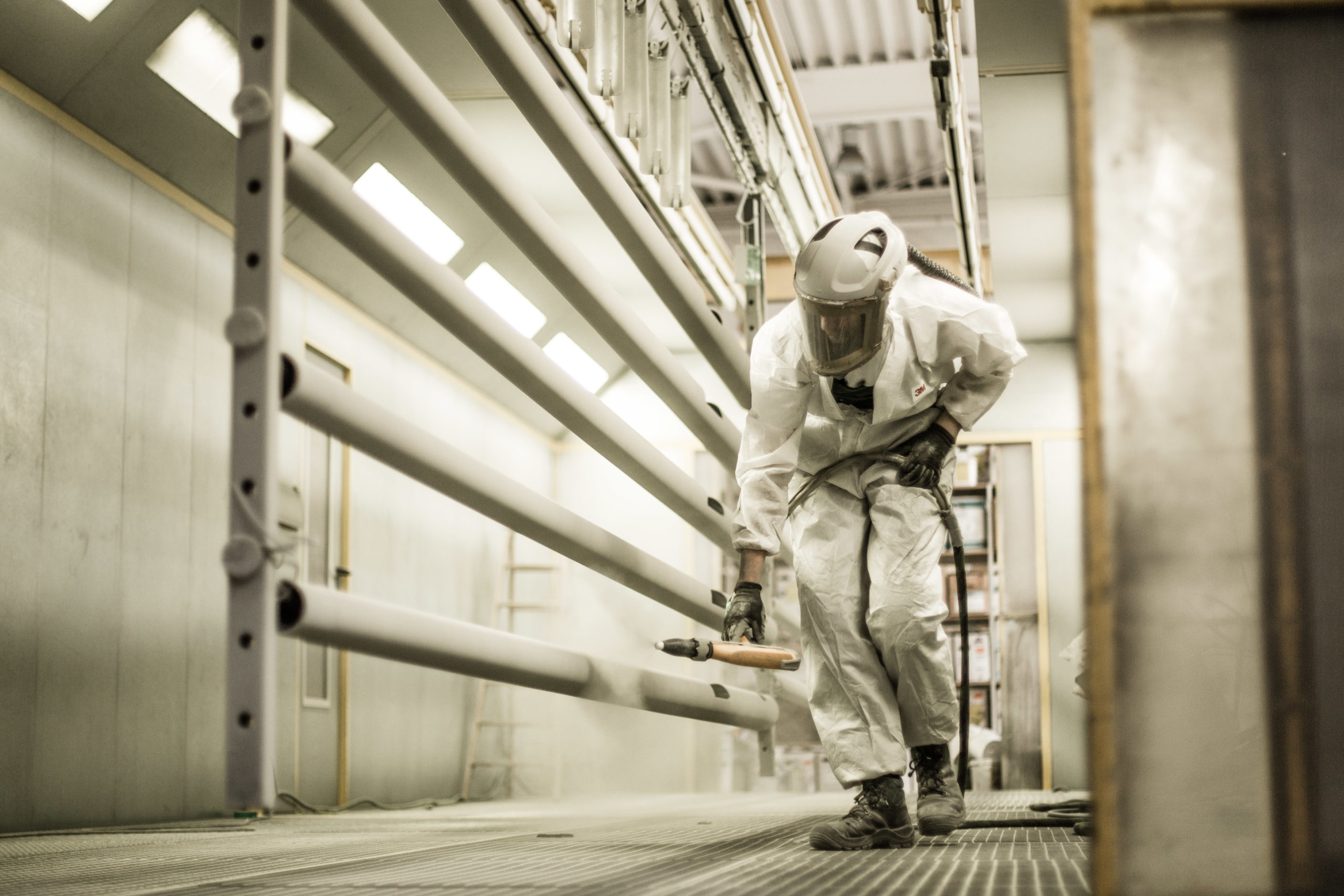 Arbeiter in Schutzkleidung spritzt Farbe auf Rohre